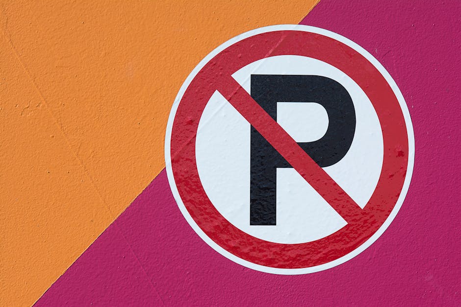 Close-up of a rusted metal gate with a wooden sign attached, displaying the handwritten message 'NO PARKING' in white paint. The gate features vertical black metal bars, some showing signs of rust and